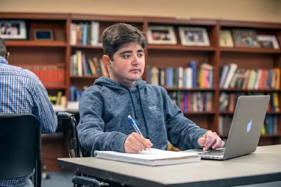 A student seated in a wheelchair works on a computer in the library.