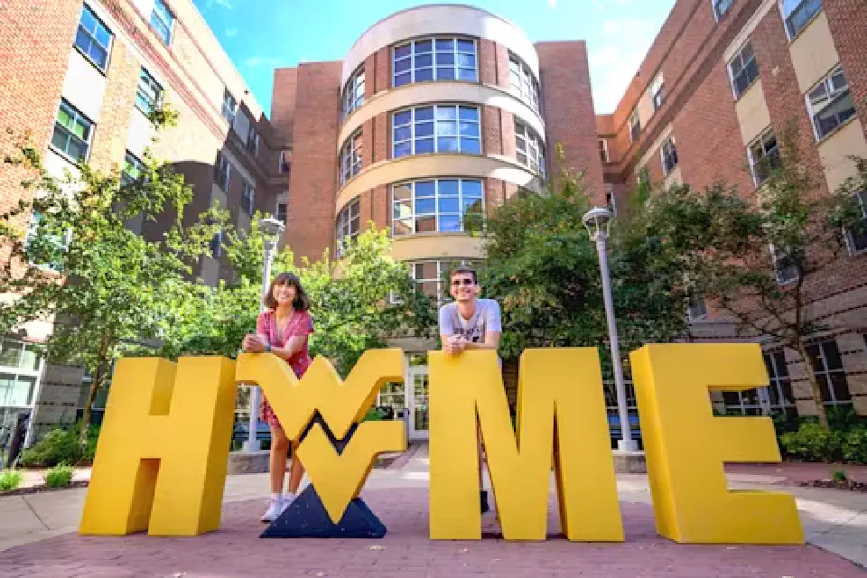 Two students pose with the Flying WV logo and giant HOME letters outside Honors Hall