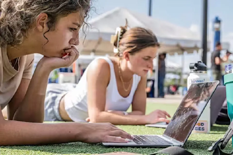 Two students use computers on the Mountainlair Green on a warm, bright day.